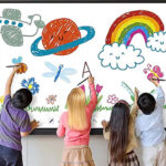 Four children drawing colorful doodles on a large interactive whiteboard showing flowers, rainbow, sun, and planets on a classroom wall.