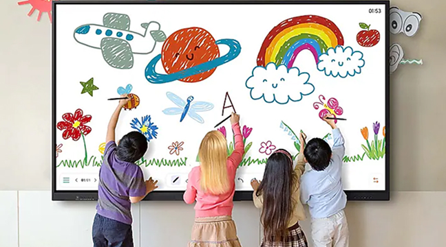 Four children drawing colorful doodles on a large interactive whiteboard showing flowers, rainbow, sun, and planets on a classroom wall.
