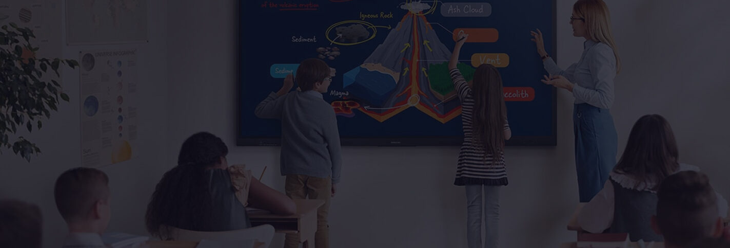 Teacher guides a science lesson as students point to a colorful cross-section diagram of earth's interior on a large screen in a classroom.