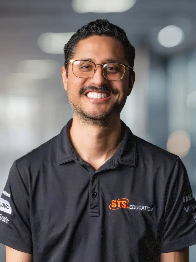 Smiling man with short dark hair and glasses wearing a black polo with STS Education logo.