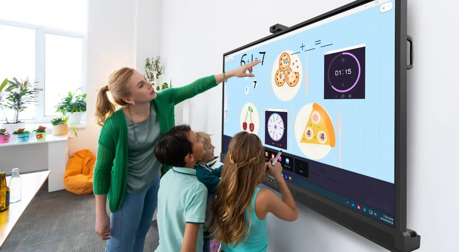 Teacher and three students engage with a large interactive whiteboard displaying math diagrams in a bright classroom.