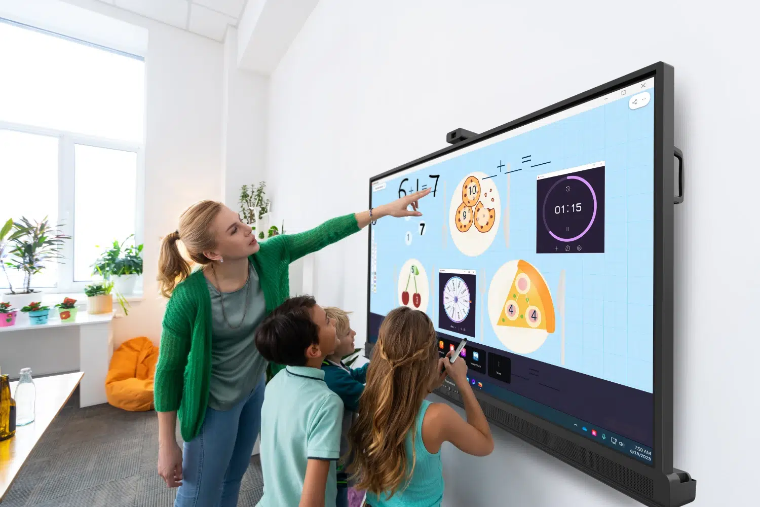 Teacher and three students engage with a large interactive whiteboard displaying math diagrams in a bright classroom.