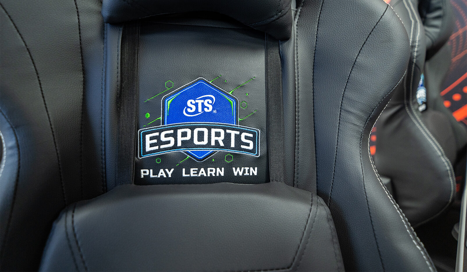 Close-up of a black gaming chair back with a blue sts esports badge and the words 'play learn win' embroidered below.