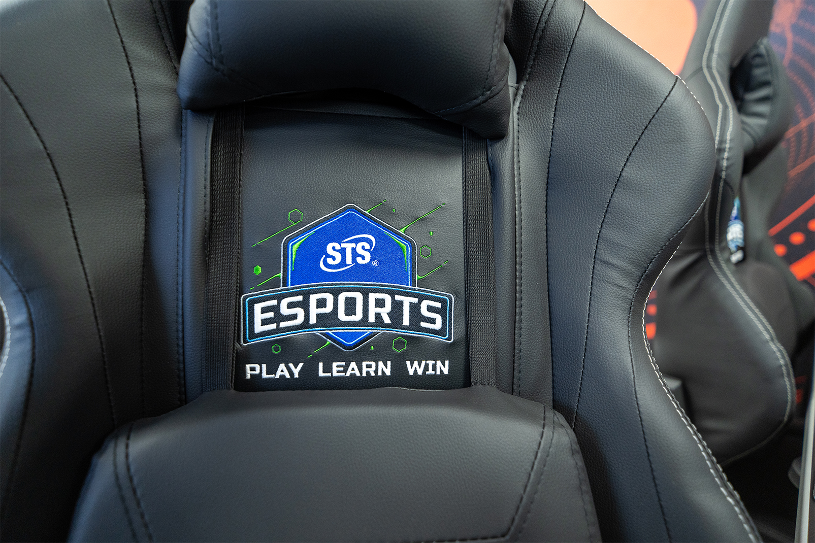 Close-up of a black gaming chair back with a blue sts esports badge and the words 'play learn win' embroidered below.
