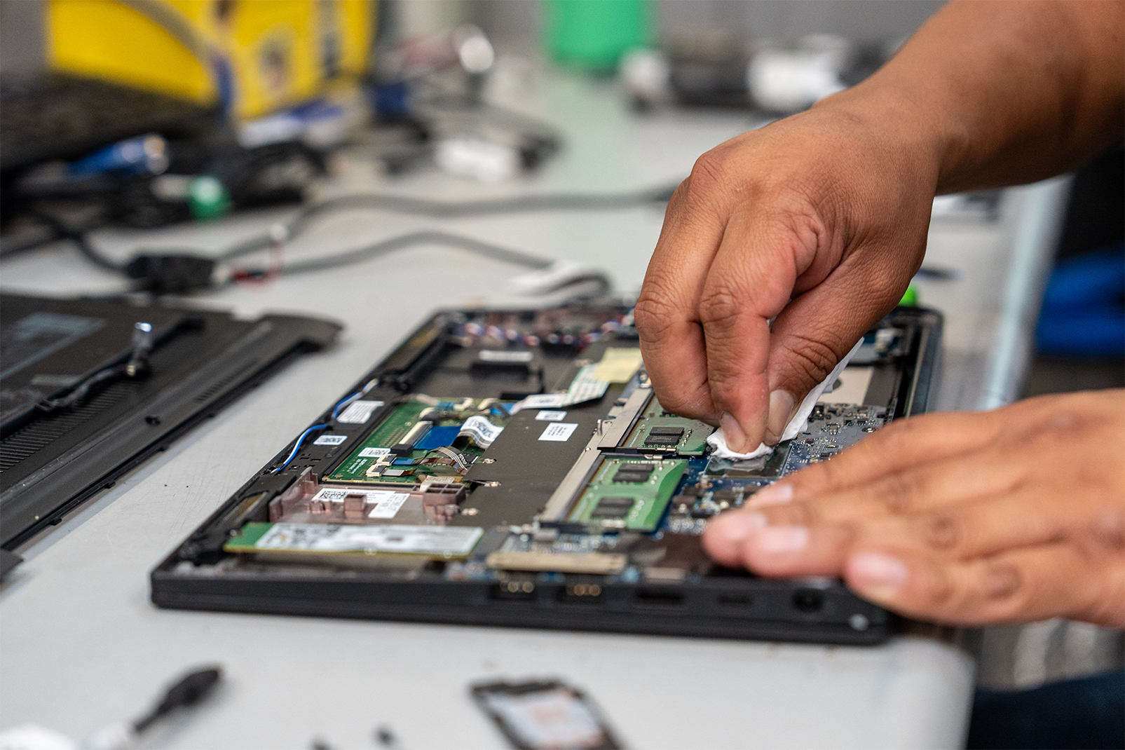 Technician cleaning a laptop's exposed motherboard on a workbench.