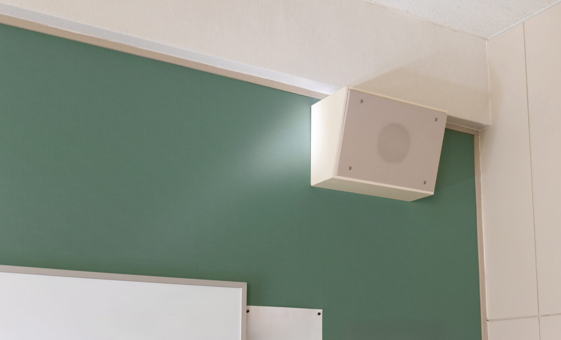 White wall-mounted speaker above a green wall panel in a classroom corner