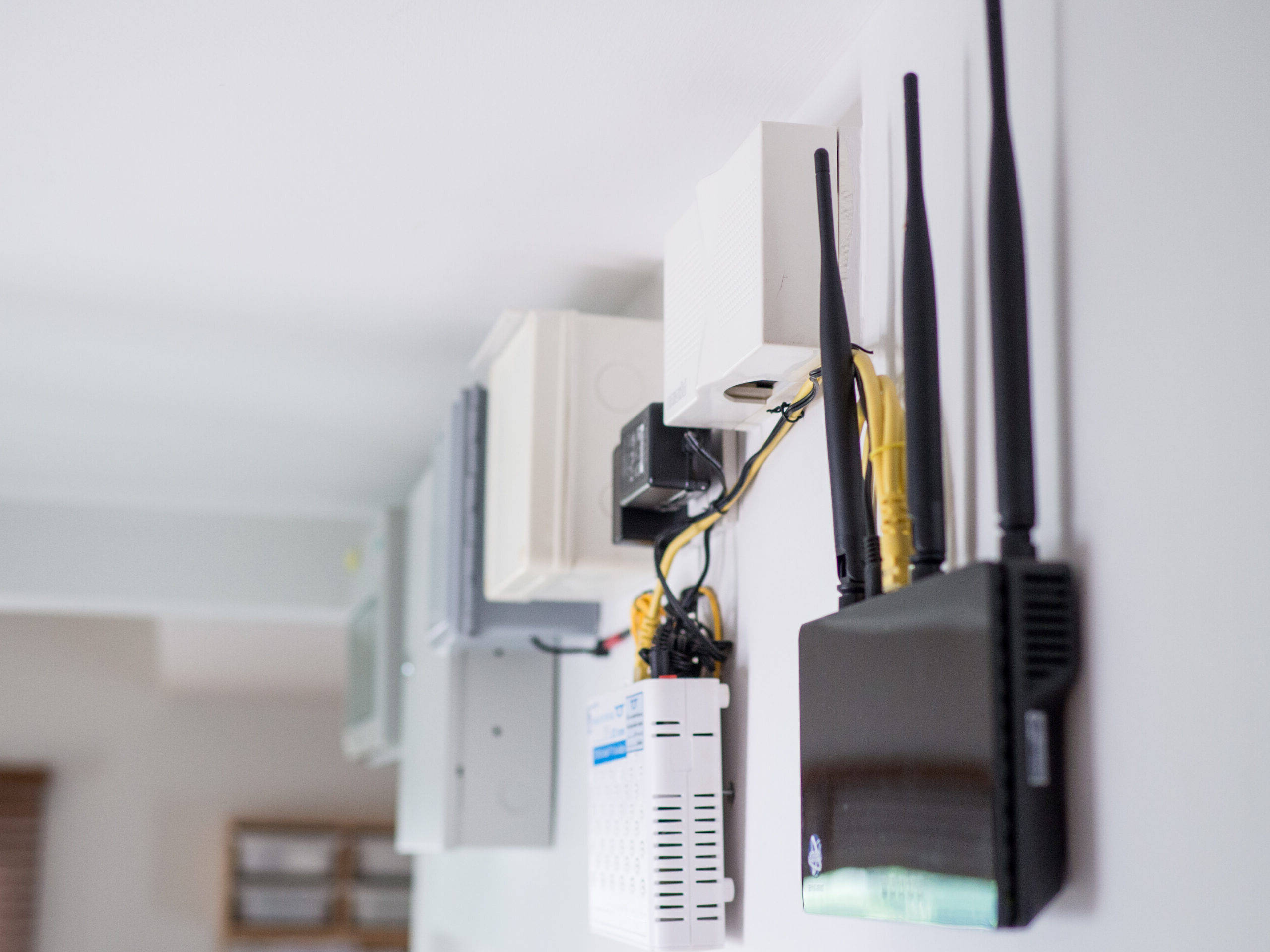 Wall-mounted networking equipment with white panels and yellow ethernet cables in an office closet