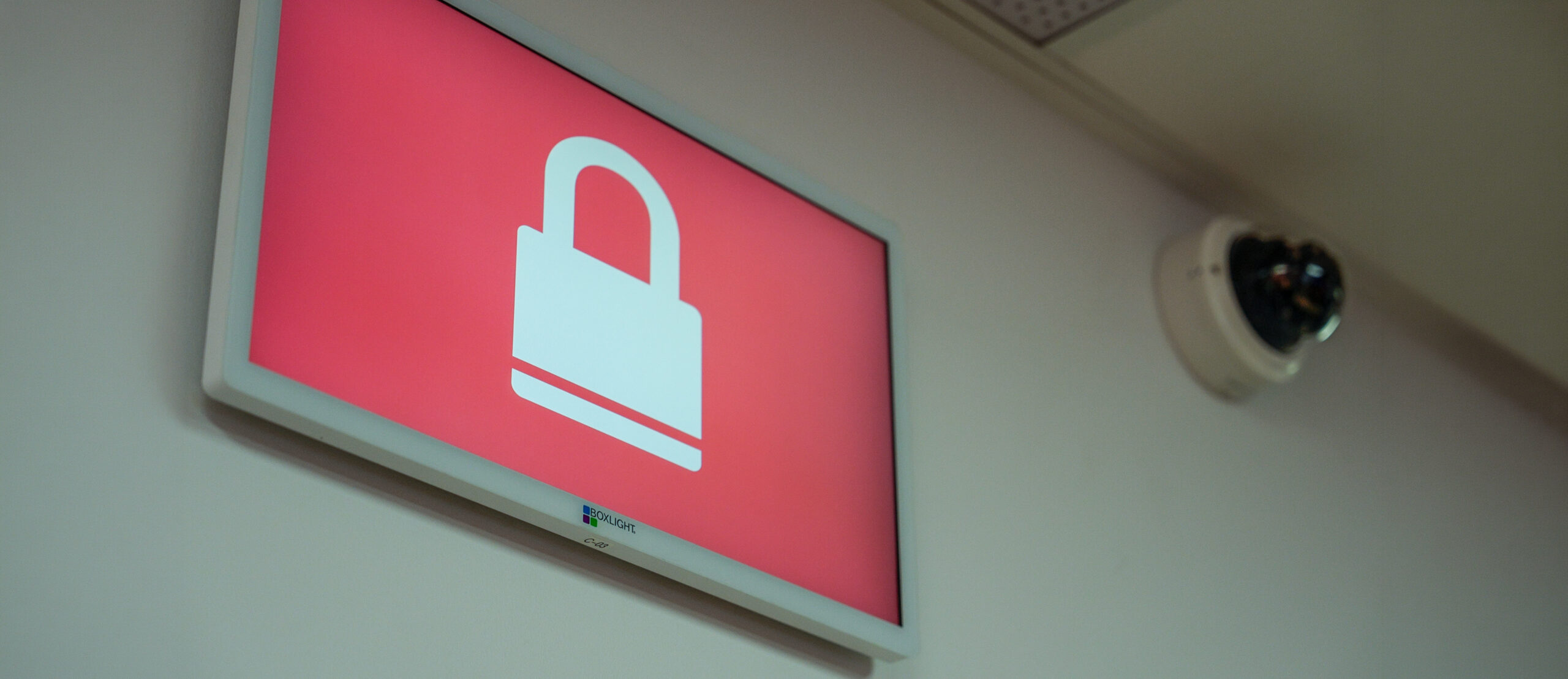 Pink wall sign with a white padlock icon indicating security or restricted access, with a security camera nearby.